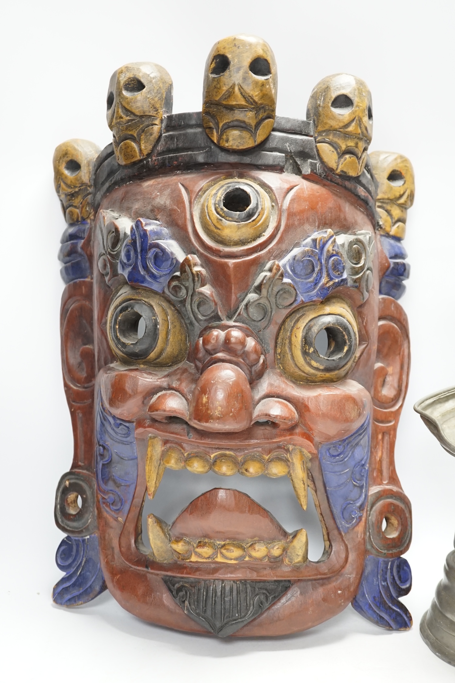 A Tibetan painted wood mask and a cast pewter candlestick, mask 44cm high